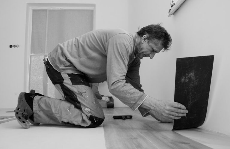 A person carries a rolled-up rug out of a room cleared for new hardwood flooring installation.