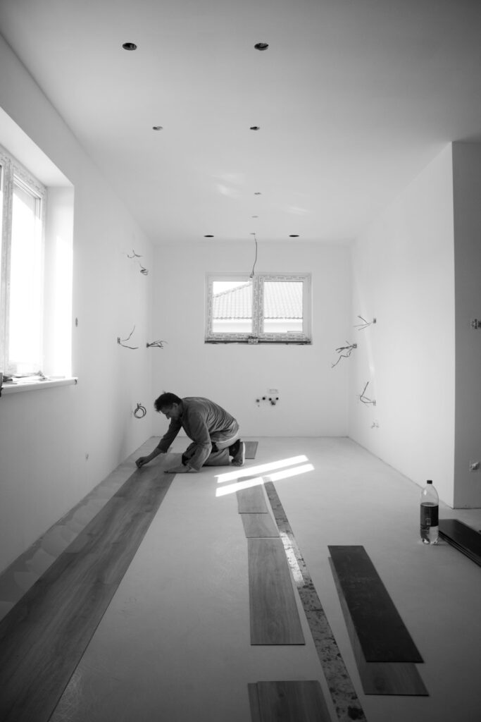 Worker measuring and installing hardwood planks in a residential living room with natural light.