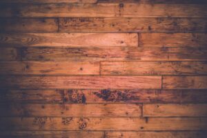 A worker uses a professional floor sander on worn hardwood in a sunny residential living room.