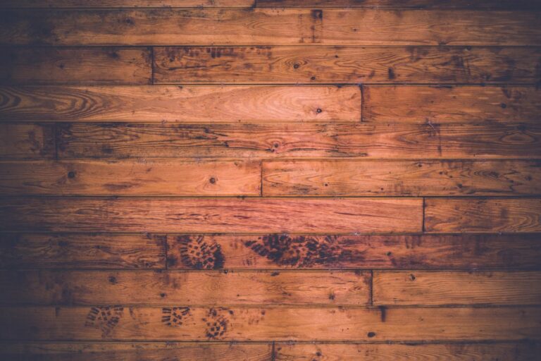 A worker uses a professional floor sander on worn hardwood in a sunny residential living room.