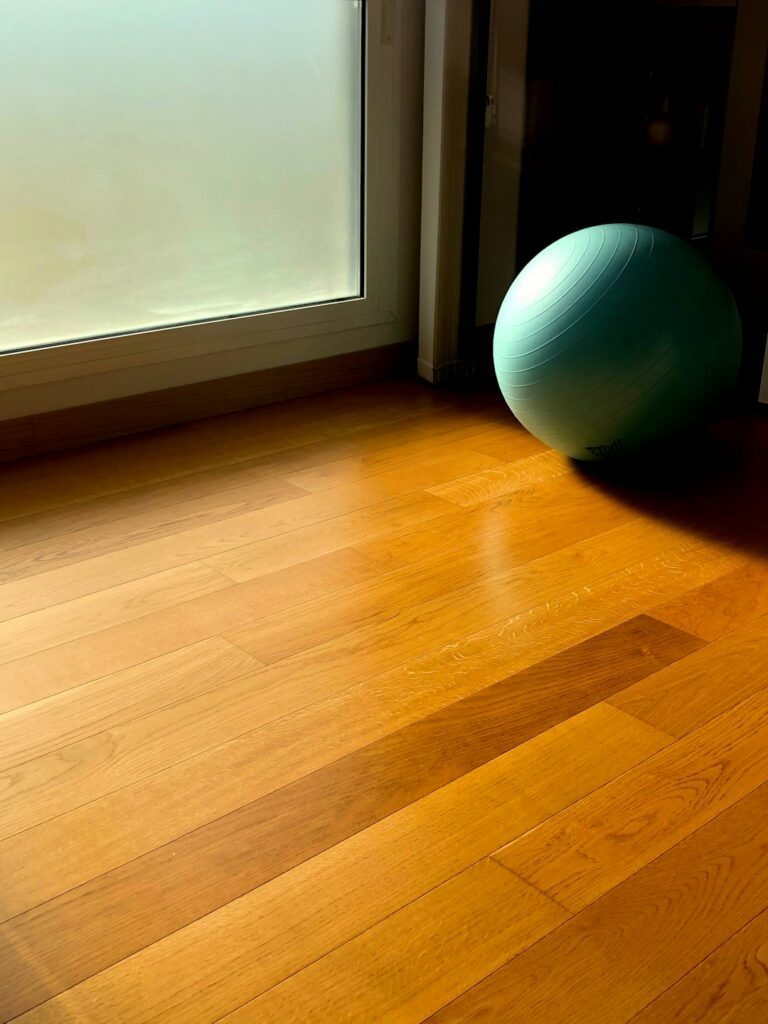 A person preparing to install engineered hardwood flooring over a clean concrete slab in a residential living room.