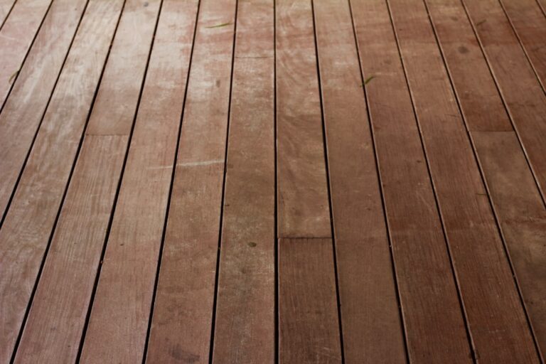 A person kneeling on hardwood flooring applying talcum powder to a visible gap between two floorboards.